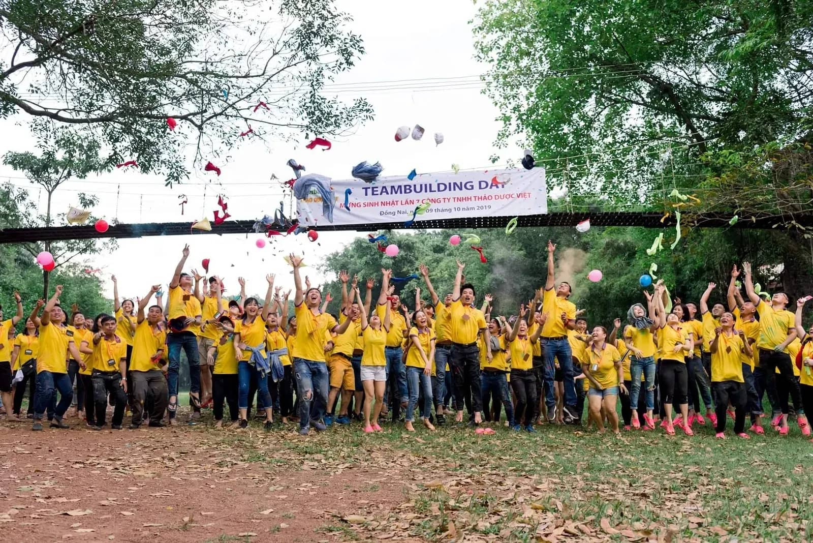 Đoàn công ty áo vàng nhảy lên chụp ảnh dưới băng rôn Teambuilding Day