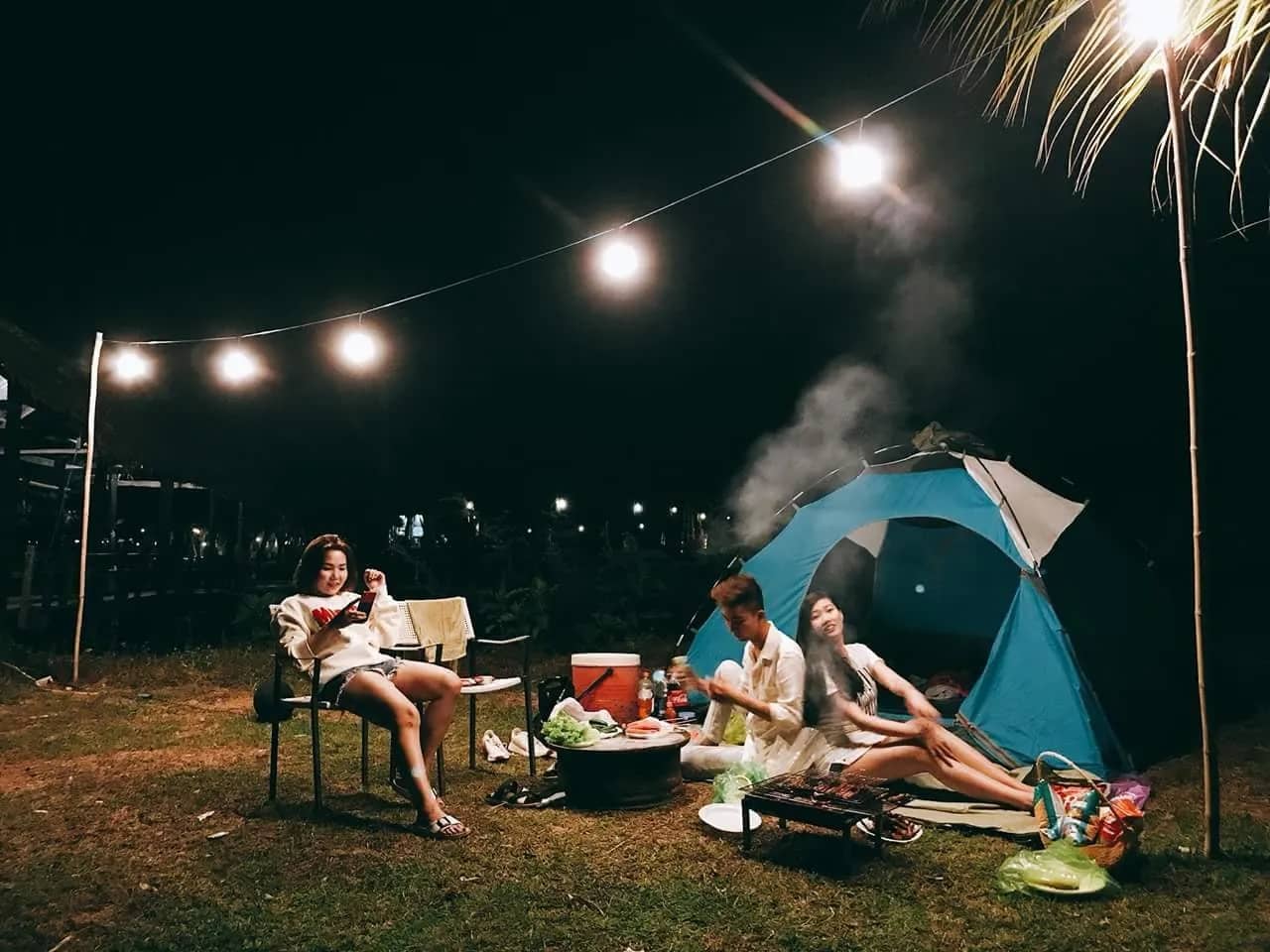 Nhóm bạn thư giãn quanh lều xanh và dây đèn trong đêm