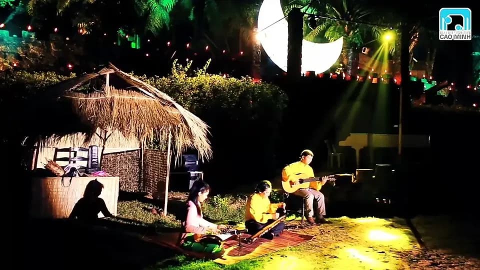 Hai người chơi guitar và hát dưới chòi lá trong đêm nhạc, đèn sân khấu rọi sáng